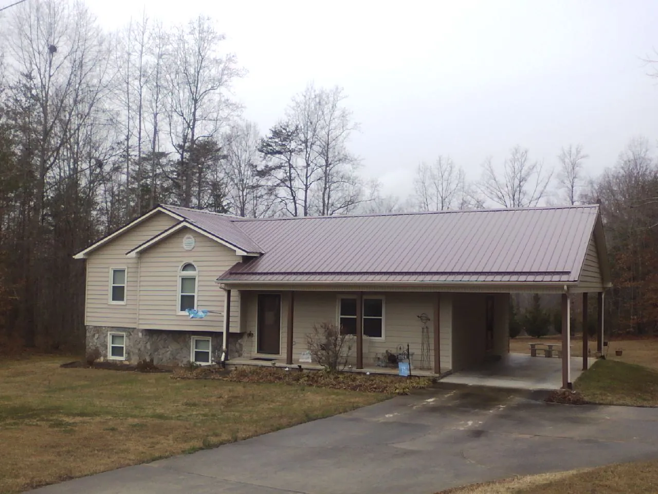 Burgundy metal roof on a tan split level home with an attached carport in Oskaloosa