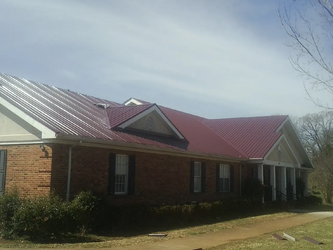 Red metal roof with gabled entries on a long brick building, from a Hail Damage Roof Repair job in Oskaloosa