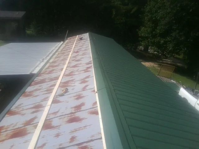 Old rusted panels beside newly installed green metal roofing — Wind Damage Roof Repair by Roofing Brothers in Oskaloosa