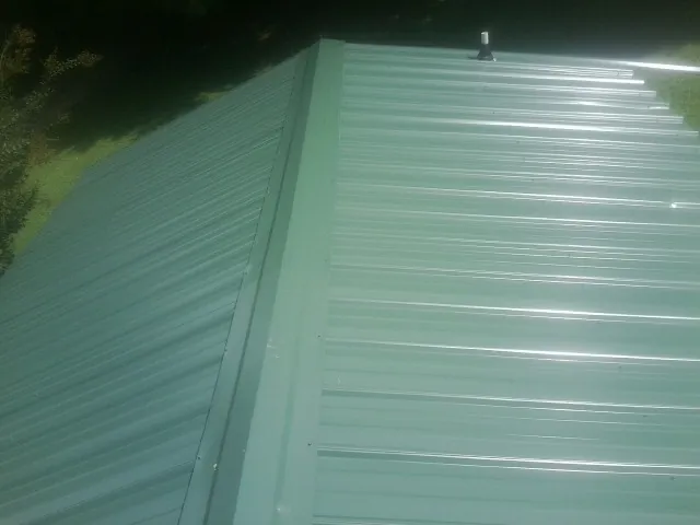 New green metal panels meeting at the ridge of a roof — Flat Roof Repair work by our crew in Oskaloosa