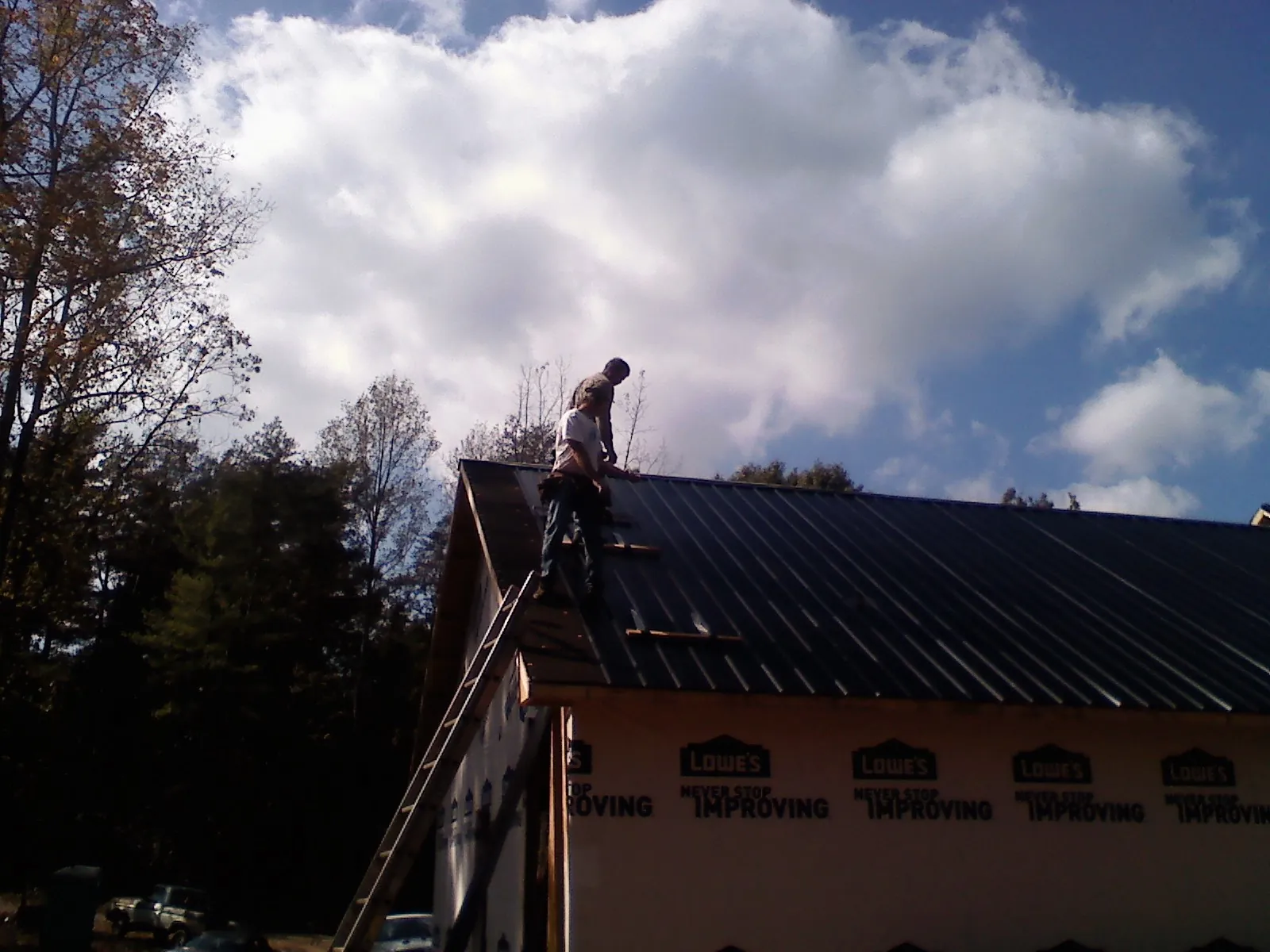 Roofer fastening dark metal panels high against a cloudy sky, from a Roof Inspection job in Oskaloosa