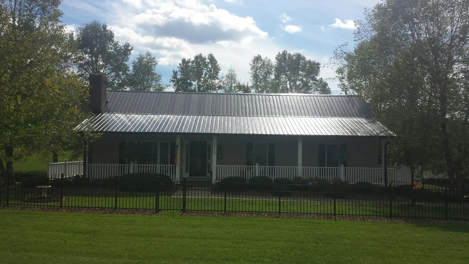 Gray metal roof on a brick ranch with a full width front porch — Gutter Guard Installation work by our crew in Oskaloosa