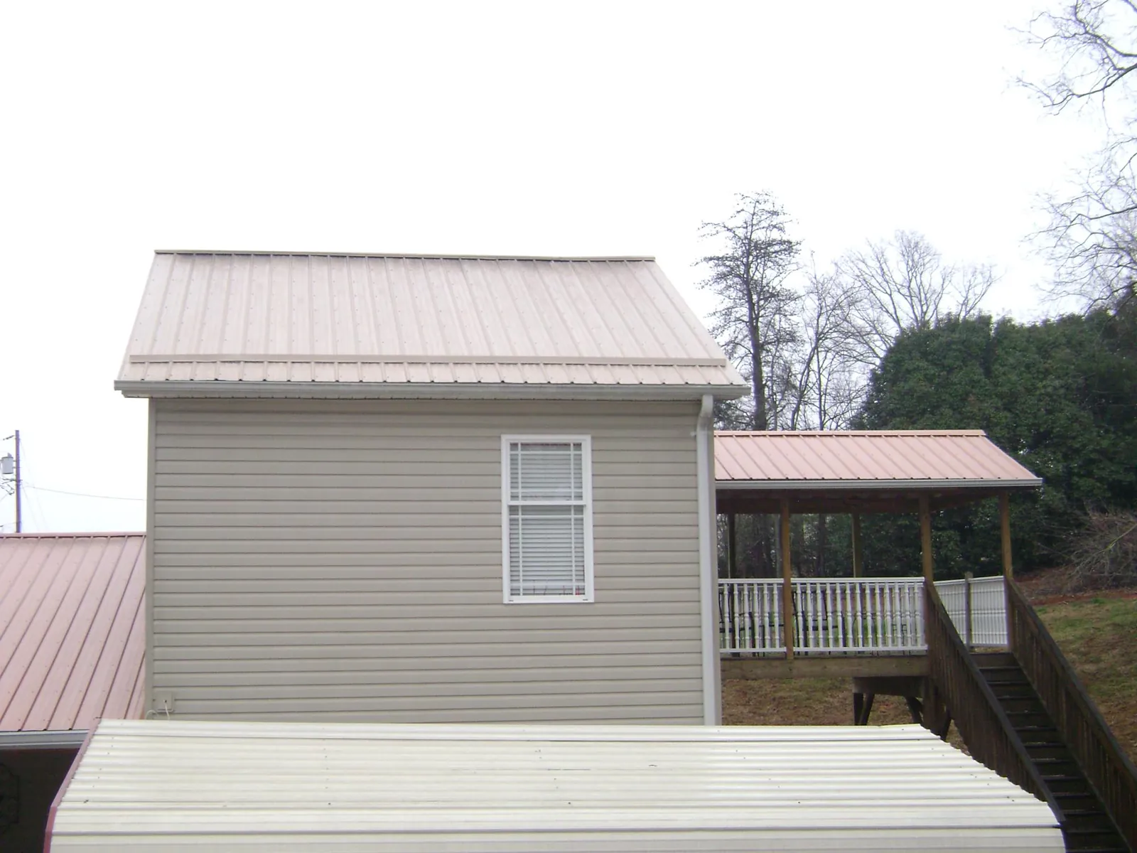 Tan metal roofs on a two story addition and attached porch, from a Roof Replacement job in Oskaloosa